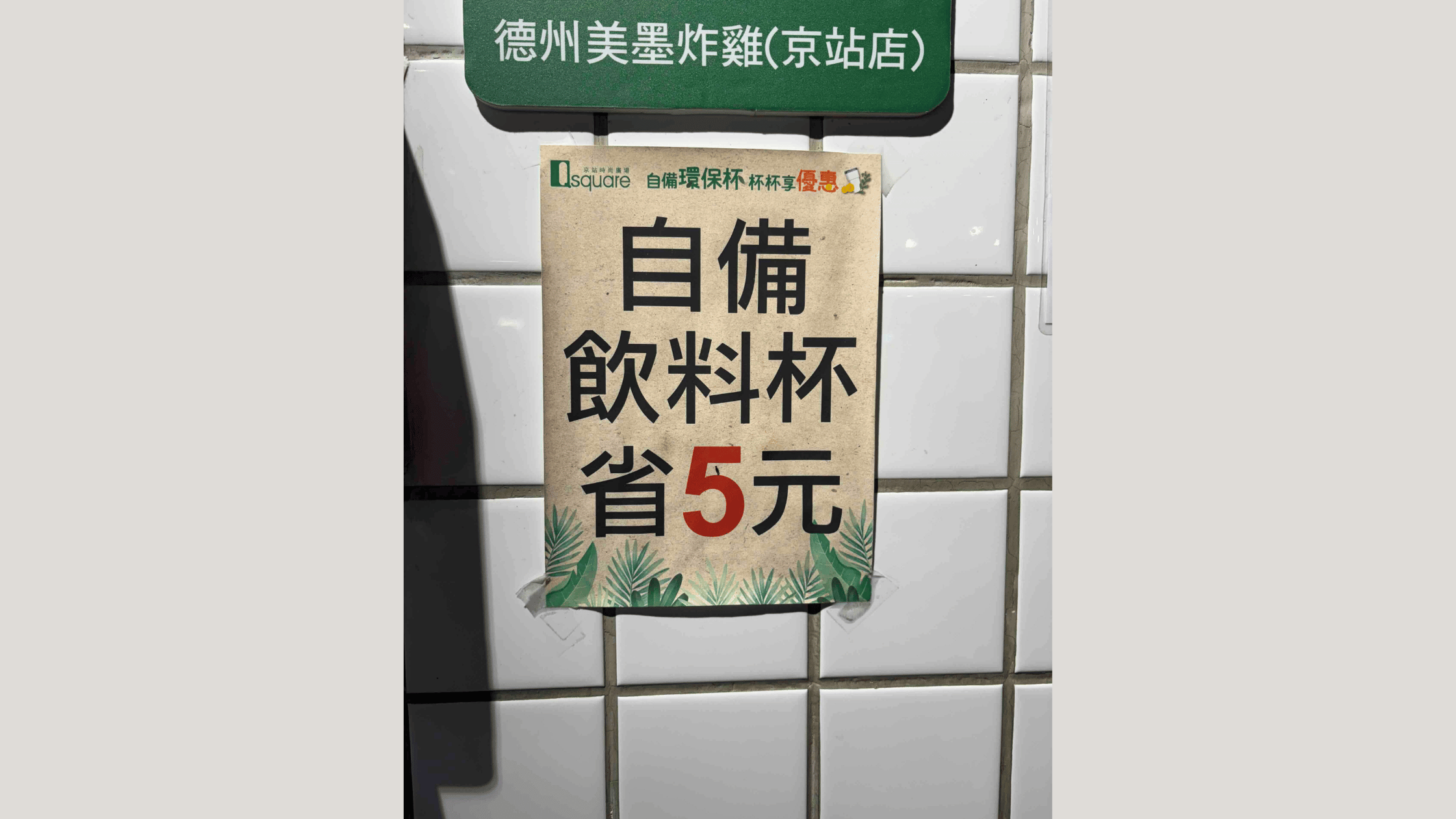 自分の飲み物用カップを持参すると5元割引になることを知らせる中国語の掲示。カフェの壁に、緑の葉の装飾が施された紙で掲示されている。